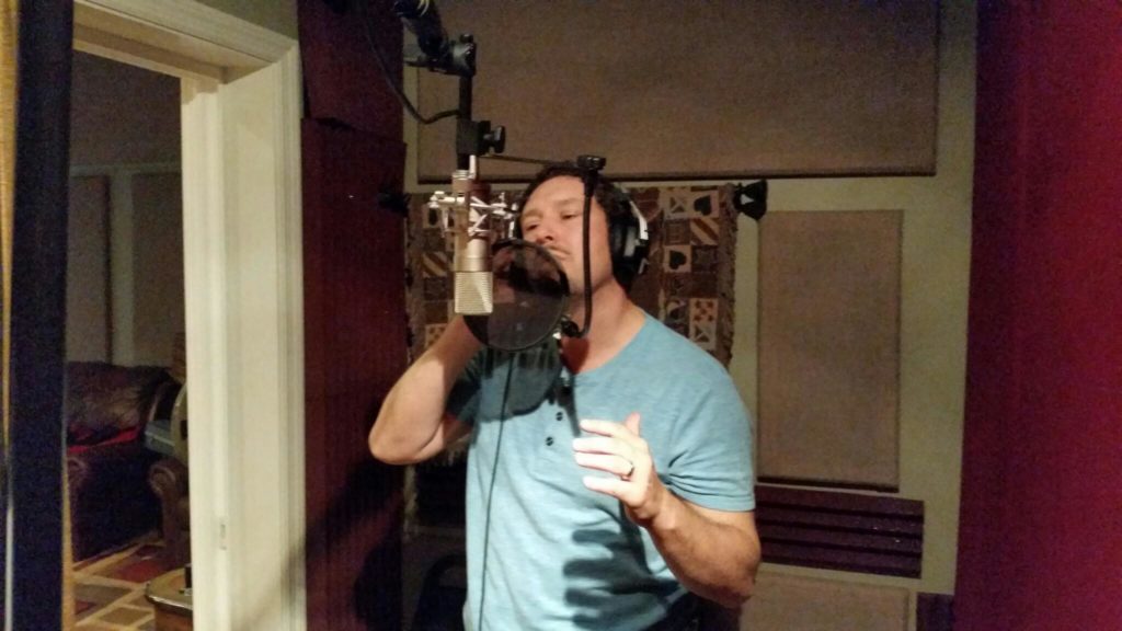 Man singing into a microphone in a recording studio.